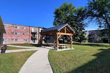 A gazebo is situated in a grassy area in front of a brick building.
